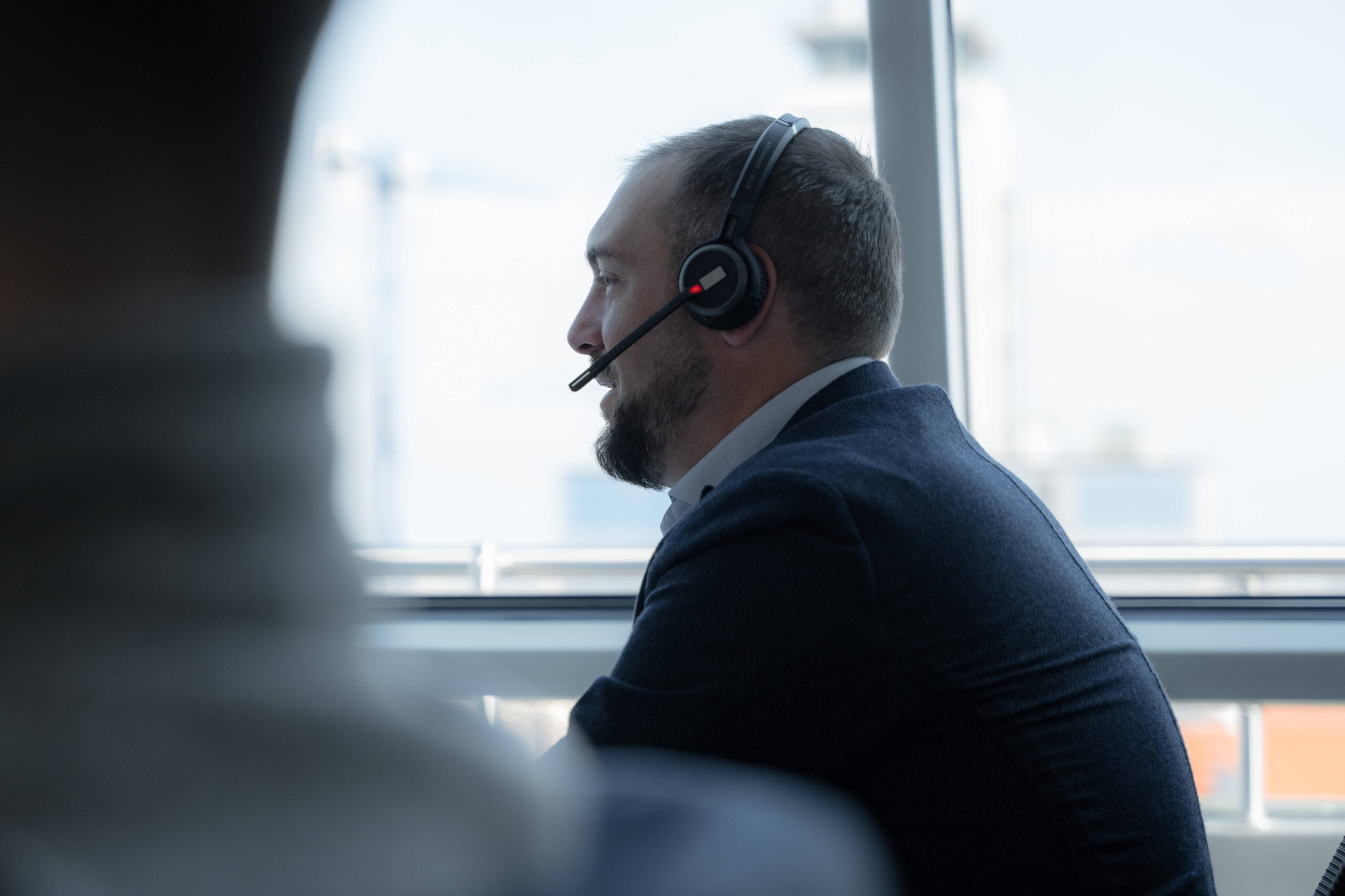 Mann im Anzug mit Headset, arbeitet an einem Schreibtisch.